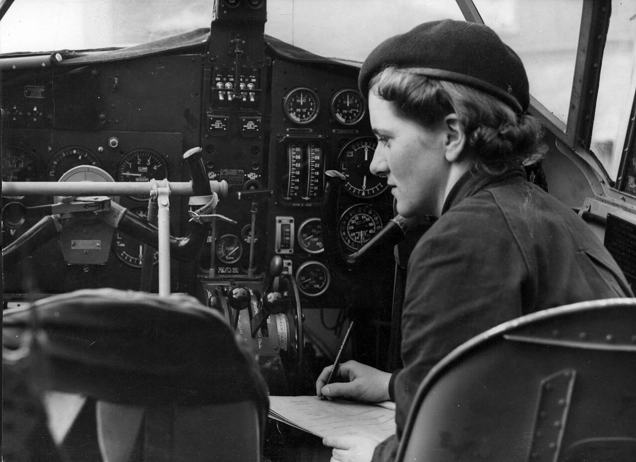 Aircraftwoman Corporal Dorothy Trewin checking the instruments in the cockpit of a bomber aircraft. She is positioned to the right of the photograph.