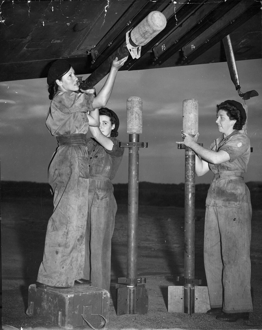 ACWs Esme Coase, Joyce Gallen and Dorothy McIntosh, load practice rockets onto a Beaufighter. All are wearing dirty boiler suits.