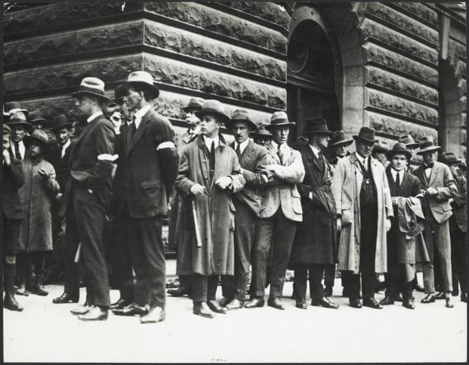 men lined up along a bluestone wall.