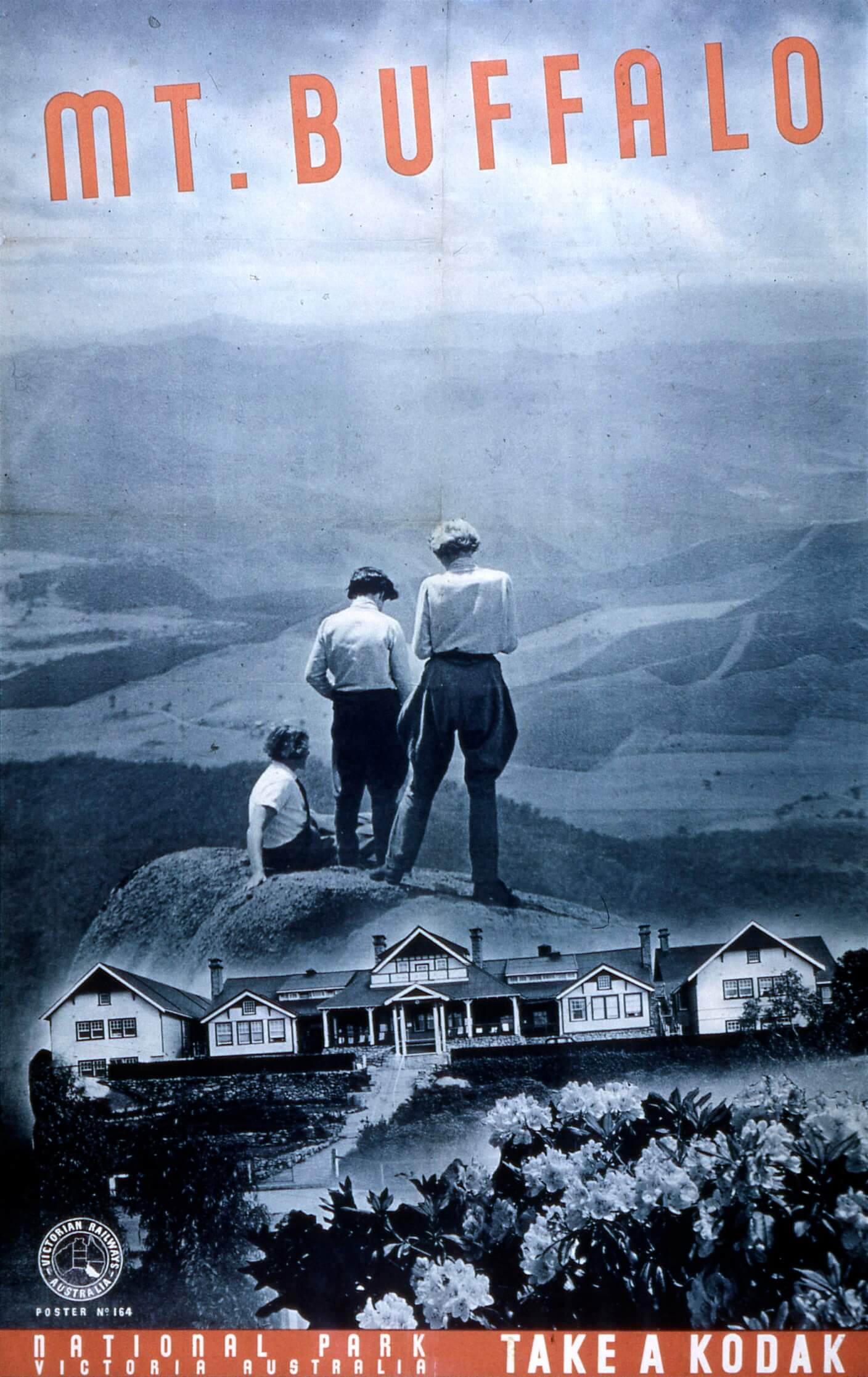 Travel poster for Mt. Buffalo is a composite image toned in blue and white with wording in a red. The upper, includes a vista looking over a mountainous range with 3 women on a hilltop or rock in the middle ground. One is sitting on the ground and 2 standing. The lower half of the image shows a sprawling ranch style building. in the lower right corner is an image of a rhododendron bush in flower.