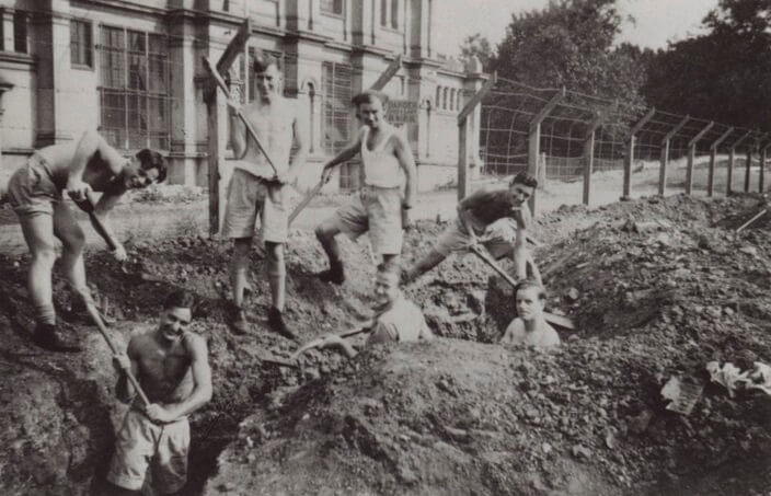Young men dig trenches outside a building. they are smiling.