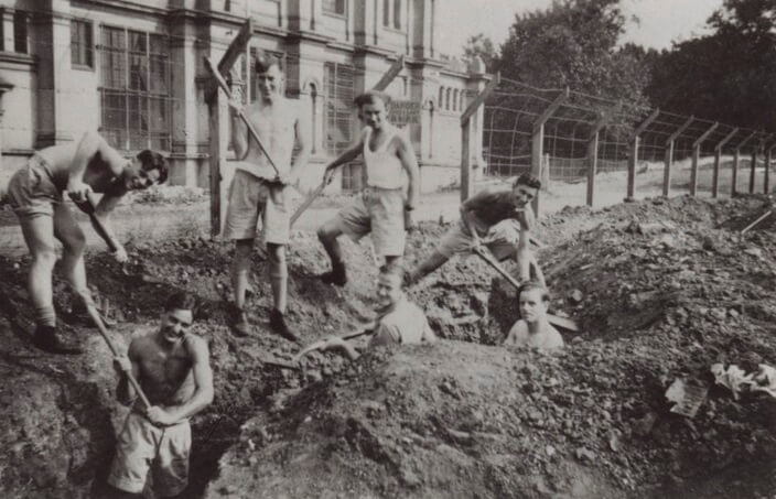 digging at the REB Young men dig trenches outside a building. they are smiling.